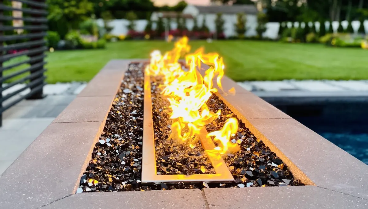 Outdoor fire feature with burning flames and glass rocks.